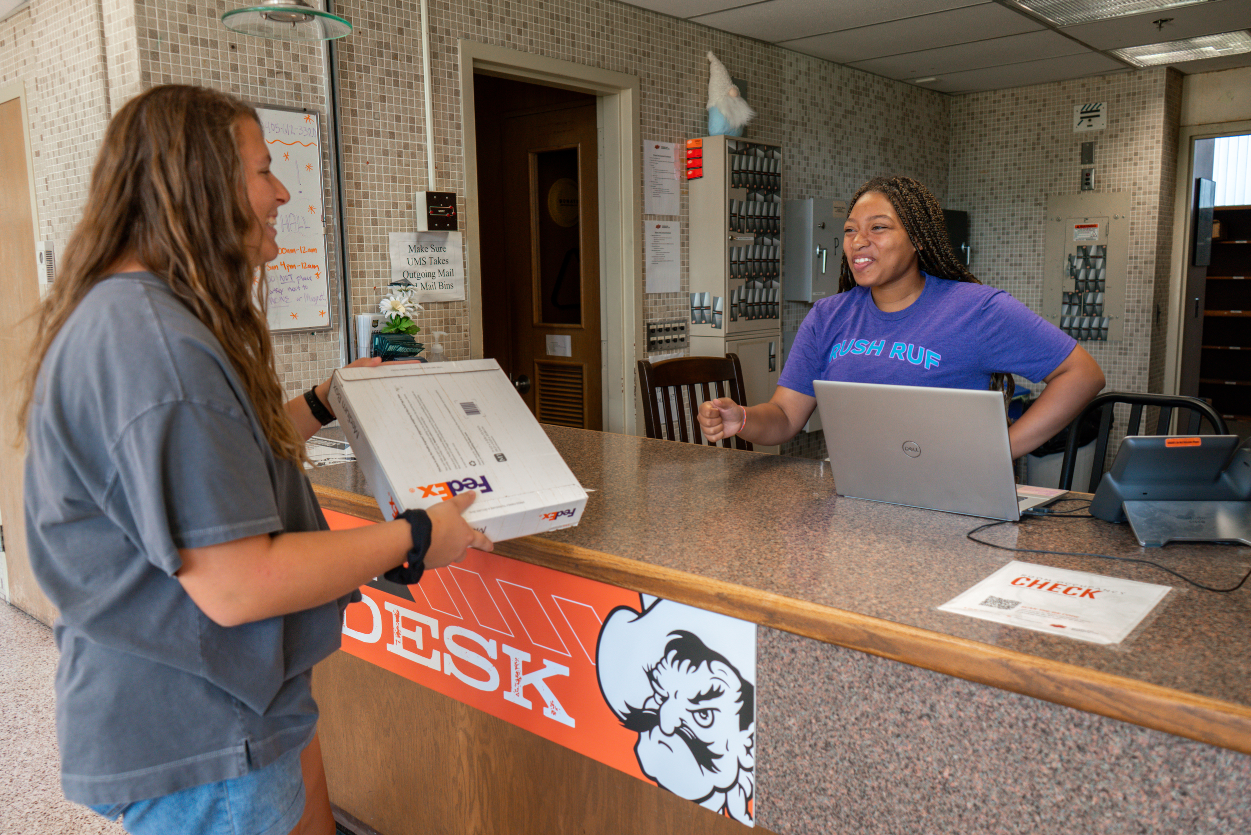 woman dropping fed-ex package off to woman behind desk