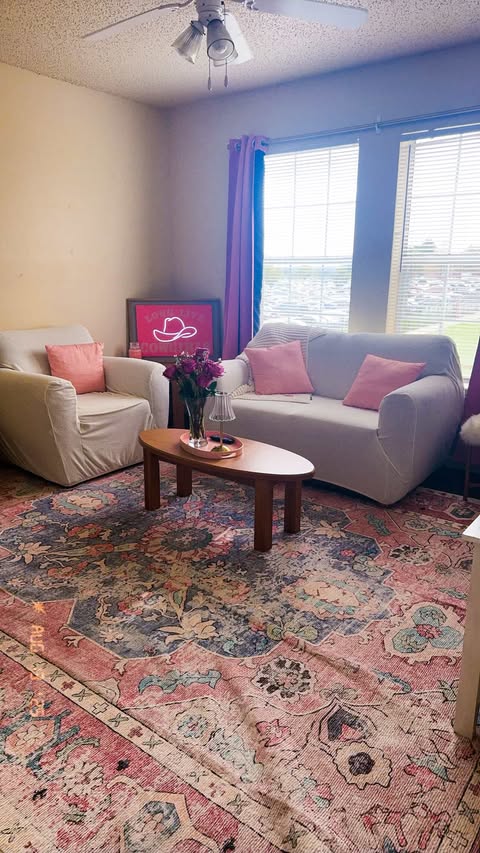 a decorated living room with grey couch covers, pink accent pillows and a cowboy hat painting.