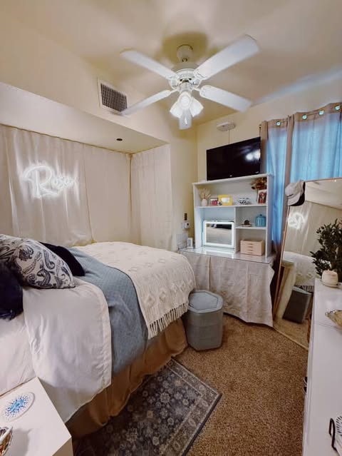 Person sitting on a bed with neutral bedding in a cozy room, with a neon sign that says 'Relax' above.