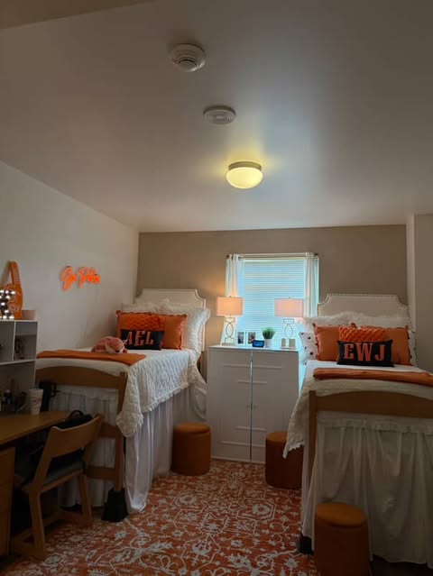 a dim lit room in the University Commons with orange decorative pillows, a glowing sign that says "go Pokes" and matching white bedding on two beds.